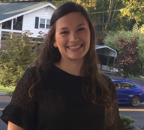 Picture of dark haired human, Haylee Mevorah-Kiehart on the porch of her old home. She is wearing black with pearl earrings. 