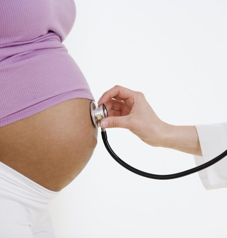 Human pregnant belly with doctor listening above navel with a stethoscope. Human wearing purple shirt and white pants. 